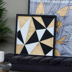 Geometric wall art with black, white, and beige triangles on a black frame, placed on a black sofa.