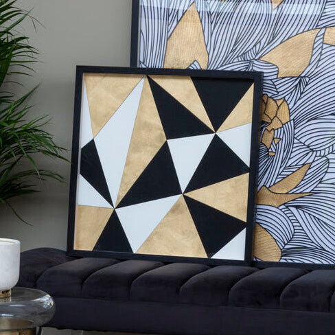 Geometric wall art with black, white, and beige triangles on a black frame, placed on a black sofa.