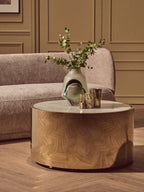Round wooden coffee table with a vase and glasses on it, in front of a gray sofa.