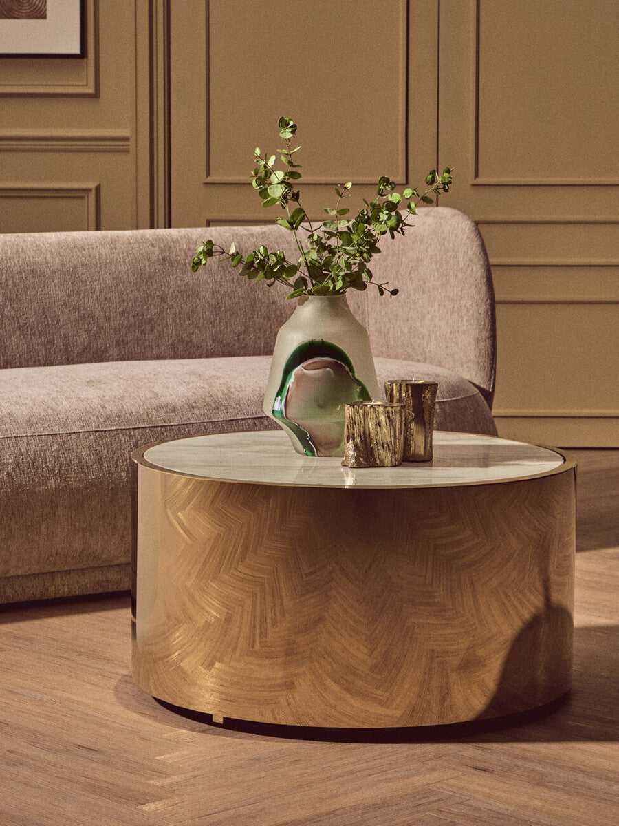 Round wooden coffee table with a vase and glasses on it, in front of a gray sofa.