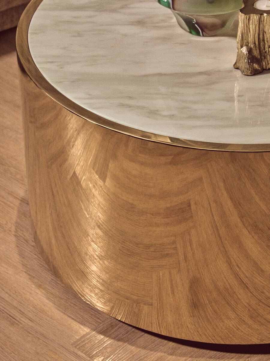 Round wooden coffee table with marble top on a wooden floor.