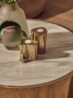 Decorative candles shaped like tree stumps on a marble table with a vase in the background.
