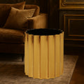 Gold side table with black top in a luxurious room with brown sofa and decorative wall.