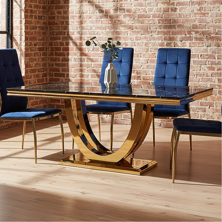 Dining table with gold legs and blue chairs against a brick wall.