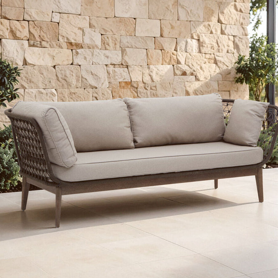 Beige outdoor sofa with cushions against a stone wall.