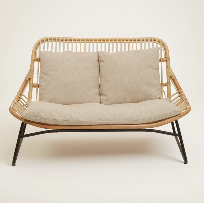 Wicker loveseat with beige cushions on a white background