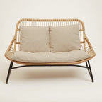 Wicker loveseat with beige cushions on a white background