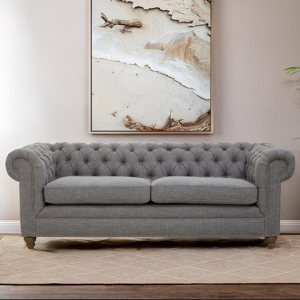 Gray tufted sofa in a room with a large abstract painting on the wall.