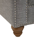 Gray upholstered chair with wooden leg and silver nailhead trim on a white background