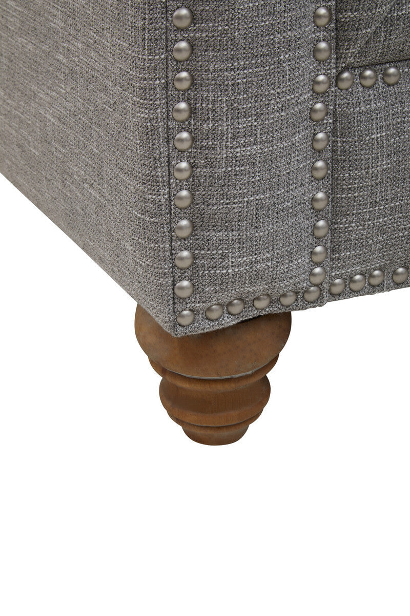 Gray upholstered chair with wooden leg and silver nailhead trim on a white background