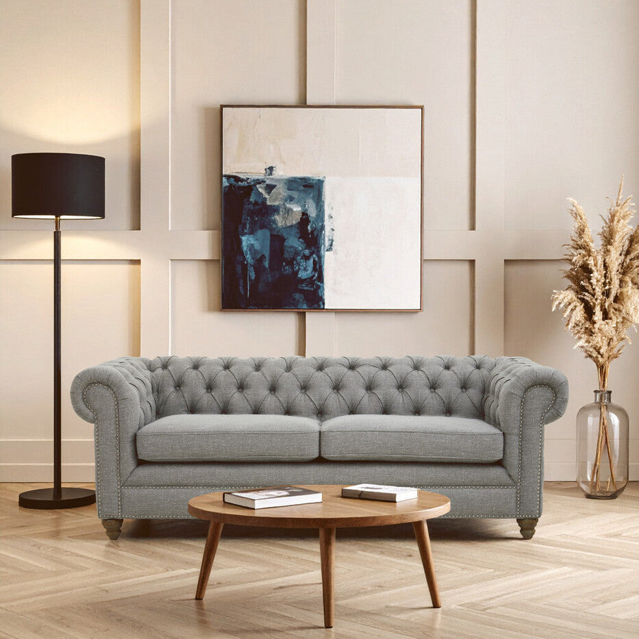 Gray tufted sofa in a living room with a wooden coffee table, lamp, and abstract painting on the wall.