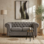 Gray tufted sofa in a living room with abstract art, lamp, and plant.