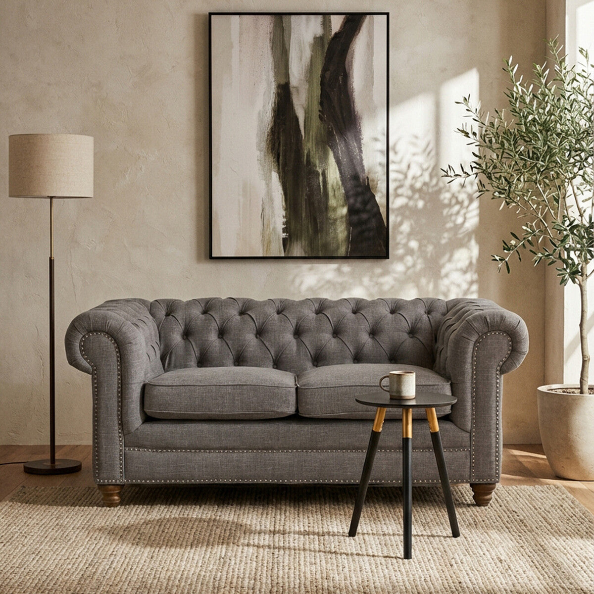 Gray tufted sofa in a living room with abstract art, lamp, and plant.