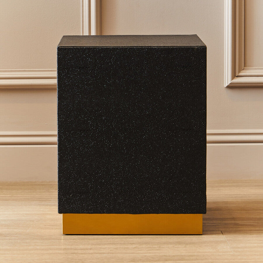 Black textured side table with gold base on a wooden floor.