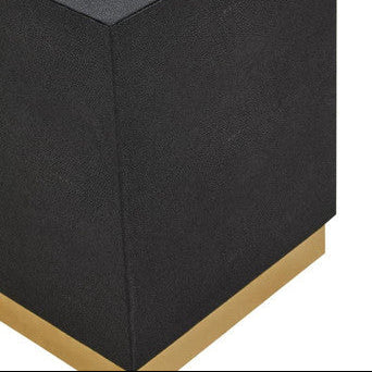 Black cube-shaped ottoman with a gold base on a white background