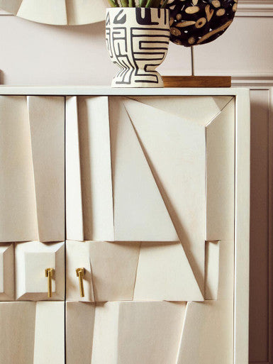 Beige cabinet with geometric design and gold handles, featuring a decorative vase on top.