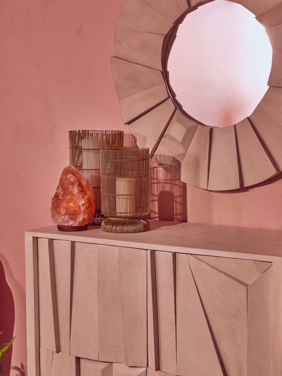 Decorative items on a table against a pink wall with a large round mirror.