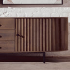 Wooden sideboard with a textured door and drawers against a light stone wall.