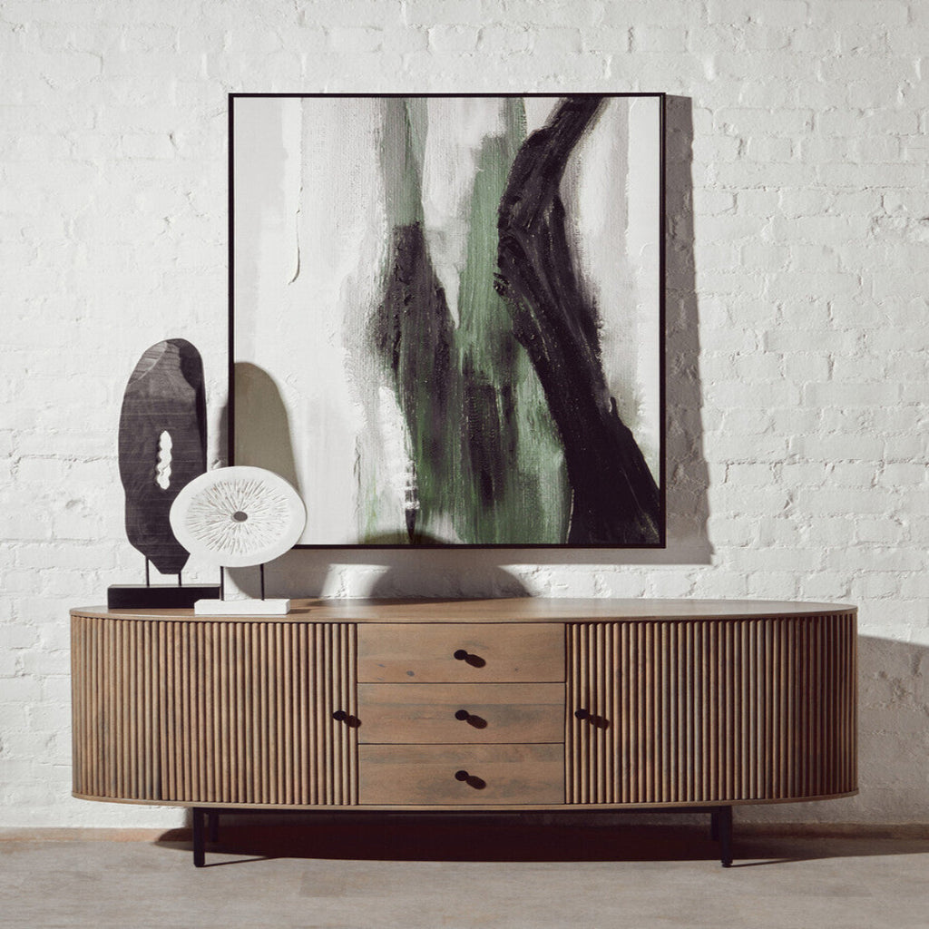 Wooden sideboard with abstract art and decorative items against a white brick wall.