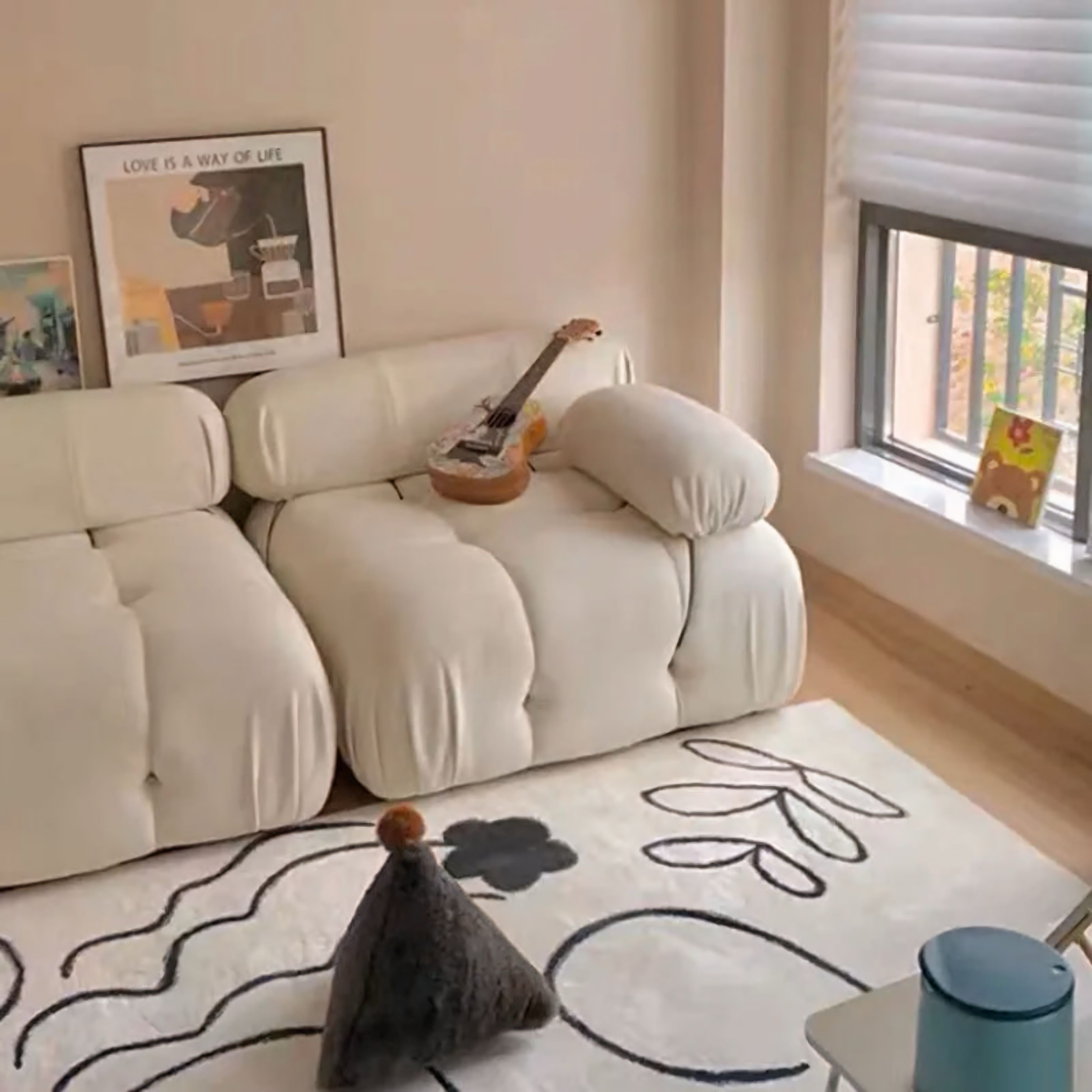 White sofa in a living room with a guitar on it, a rug with abstract designs, and a window in the background.