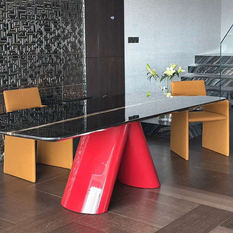 A modern dining table with a glossy black glass top and a bold red sculptural base, surrounded by mustard yellow chairs in a contemporary interior setting.