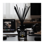 Black diffuser with sticks on a desk with a laptop and camera in the background