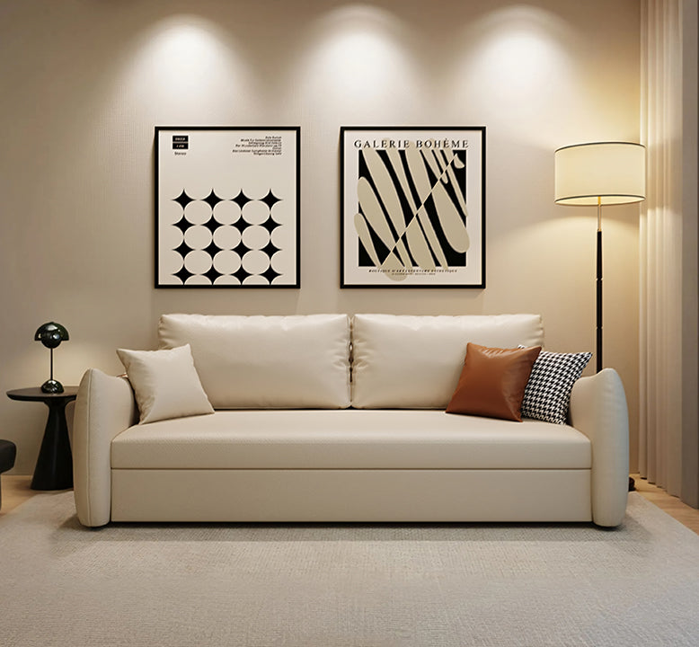 Beige sofa with decorative pillows in a living room setting with framed art and a lamp.