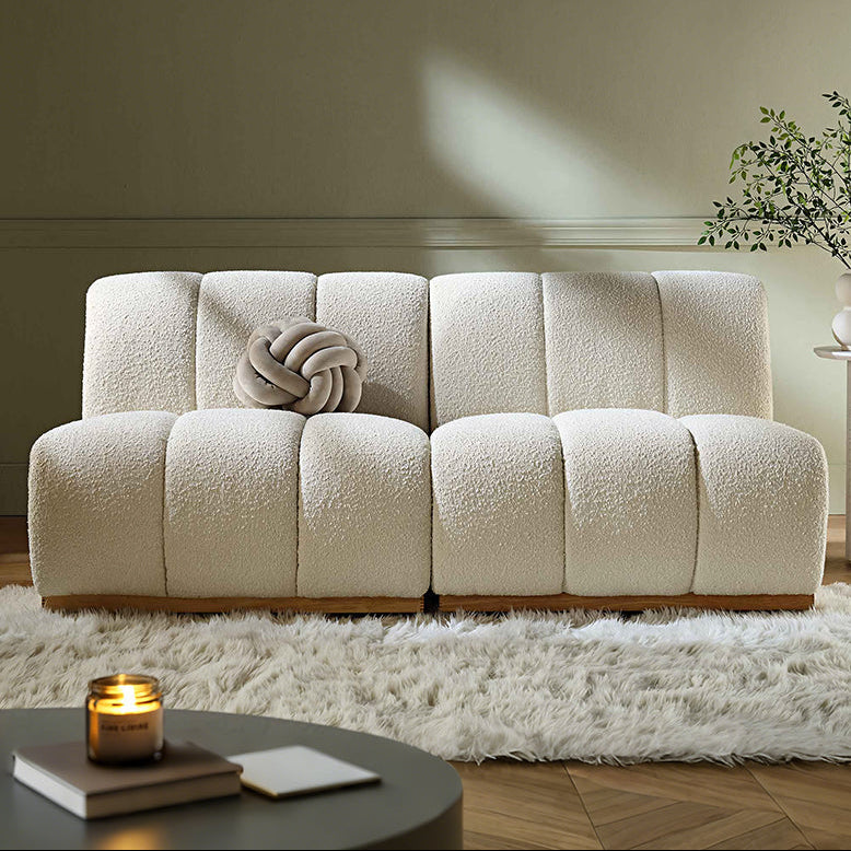 Beige sofa in a living room setting with a candle and plant on a table.
