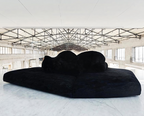 Black sofa in a large, open warehouse with high ceilings and large windows.