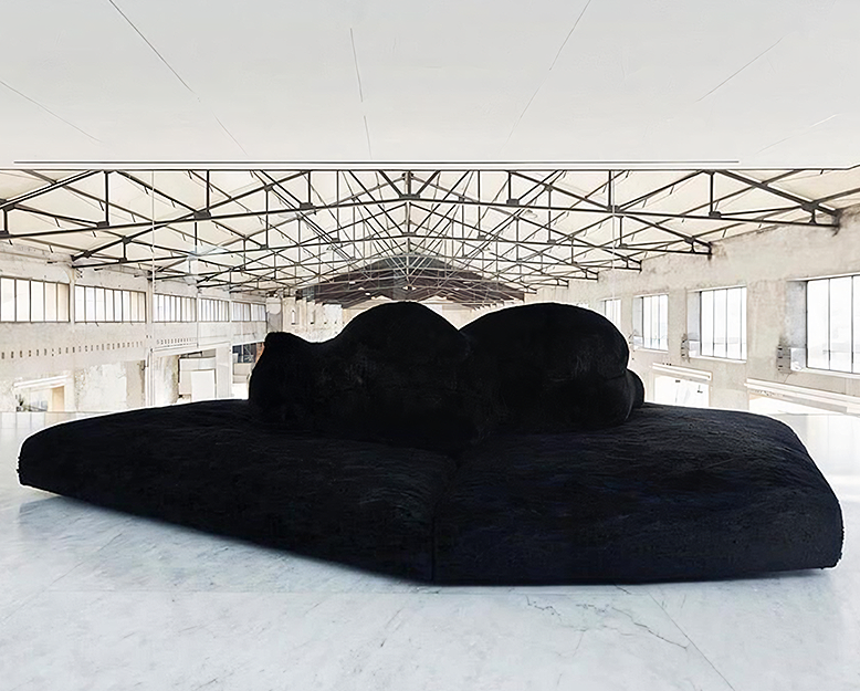 Black sofa in a large, open warehouse with high ceilings and large windows.