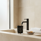 Black candle with 'PARKS' branding on a bathroom counter next to a faucet and towels.