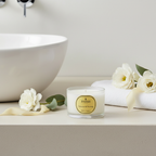 Candle with a 'Parks' label on a bathroom counter with flowers and a towel.