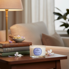 Candle on a table with books and a bowl of flowers in a cozy living room setting.