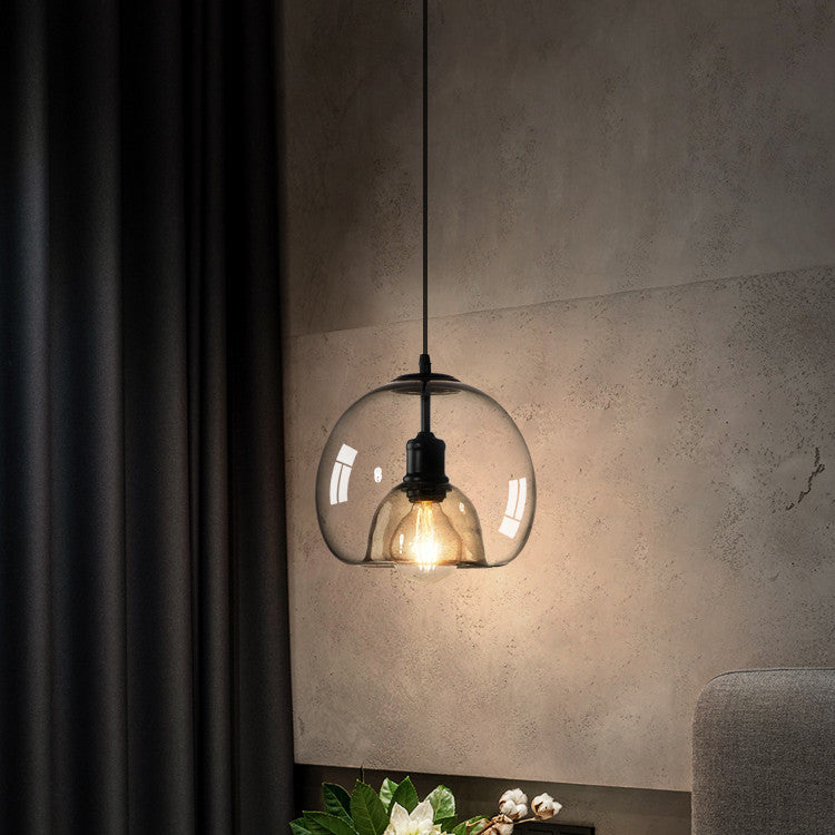 Glass pendant light hanging against a textured wall with a plant and chair in the background.