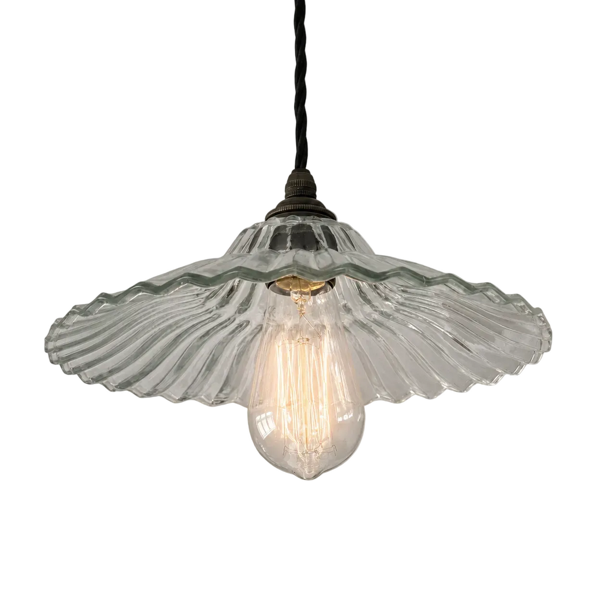 A vintage-style pendant light with a clear ribbed glass flower or scallop shade and a visible glowing bulb inside, hanging from a black cord against a plain light gray background.