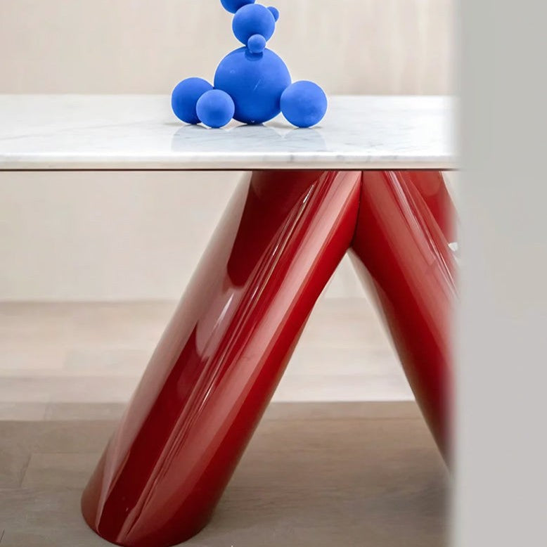 A modern table with a glossy red V-shaped base and a white marble top, styled with a blue sculptural bear figurine on a light wood floor.