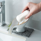 Hand using a white soap bar with gold accents on a decorative soap dish.