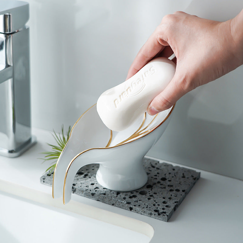Hand using a white soap bar with gold accents on a decorative soap dish.