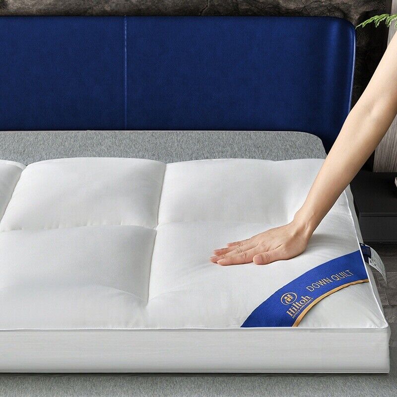 Person touching a white mattress topper with a brand label on a bed.