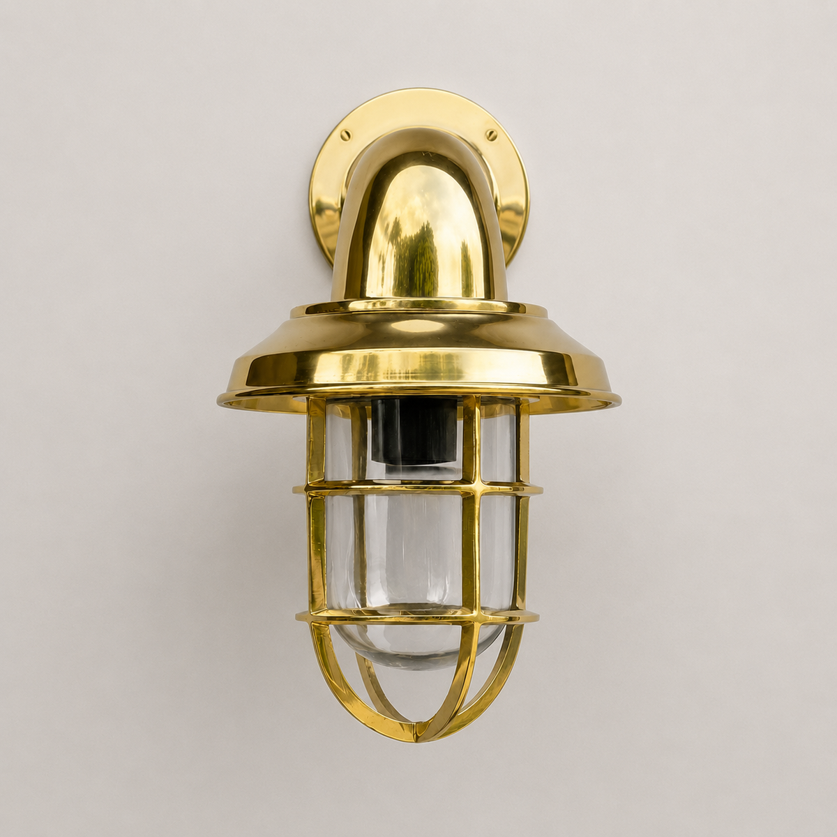 Brass wall-mounted light fixture with glass cover on a gray background