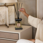 Person adjusting a diffuser on a nightstand with a lamp in the background