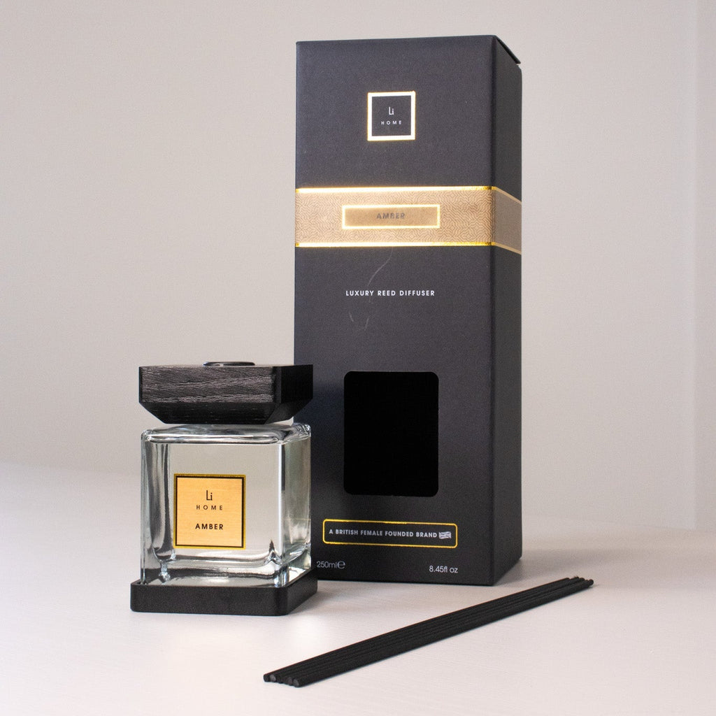 A black and gold scented candle with packaging on a white background