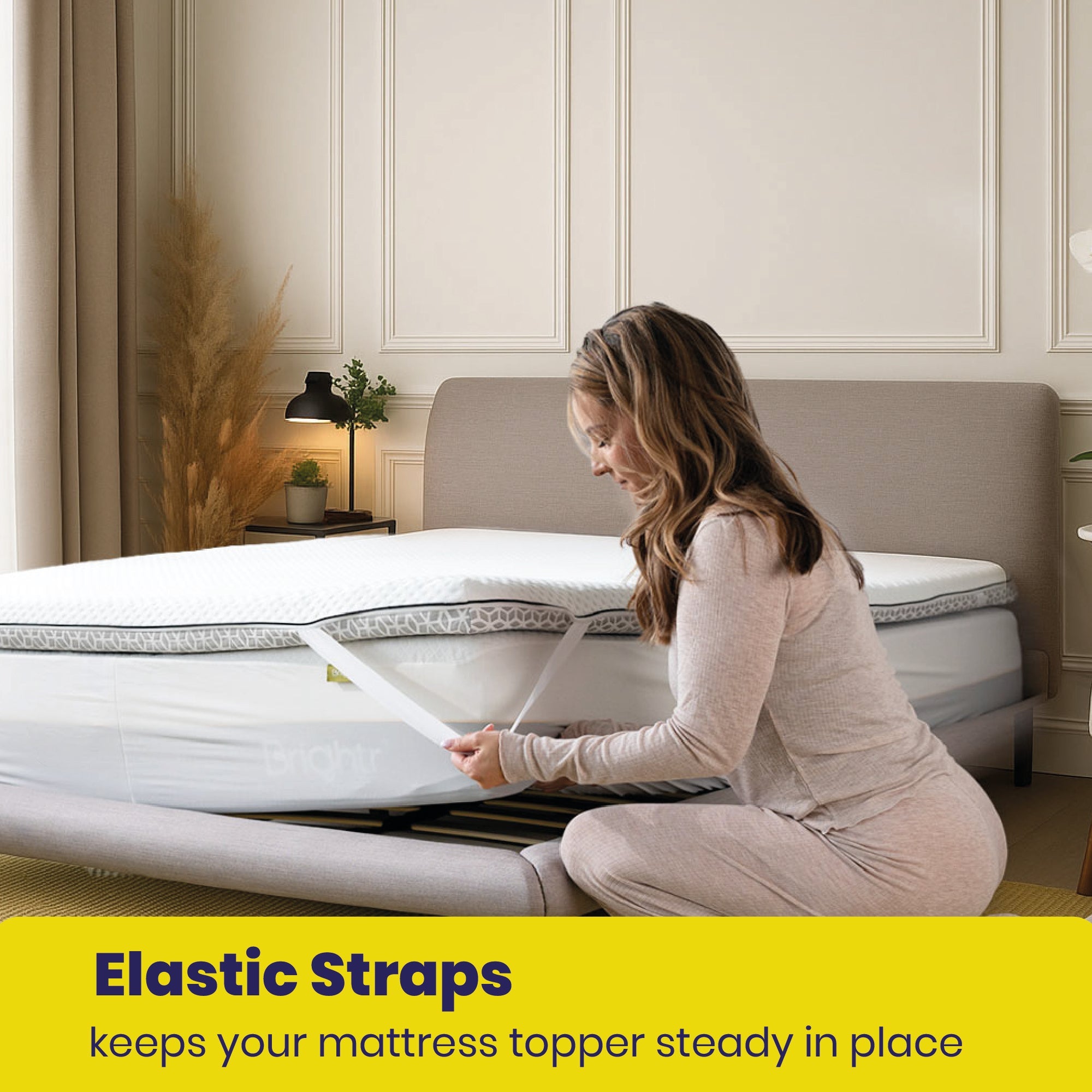 Woman adjusting a mattress topper with elastic straps in a bedroom setting.