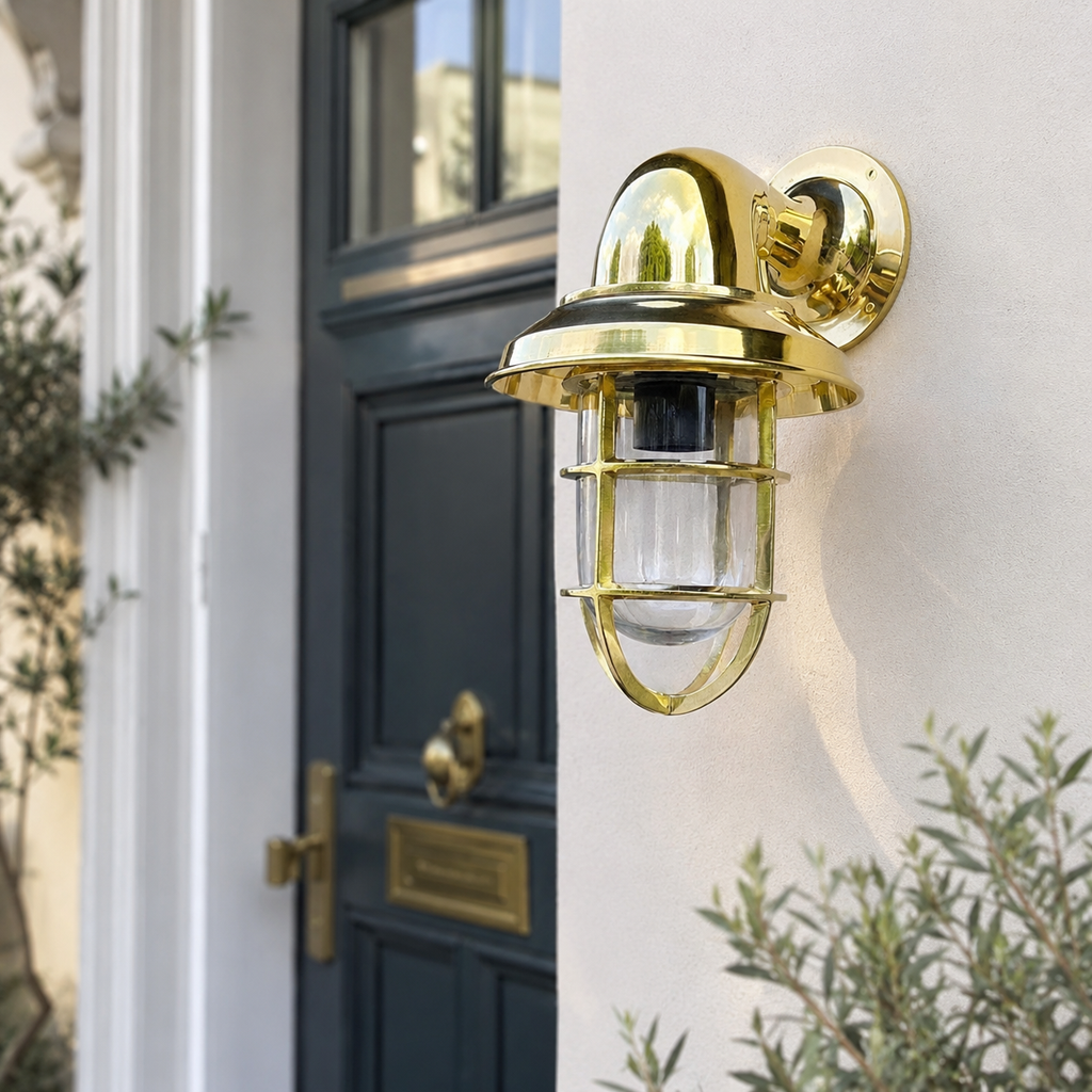 Gold outdoor wall light fixture on a white wall next to a black door.