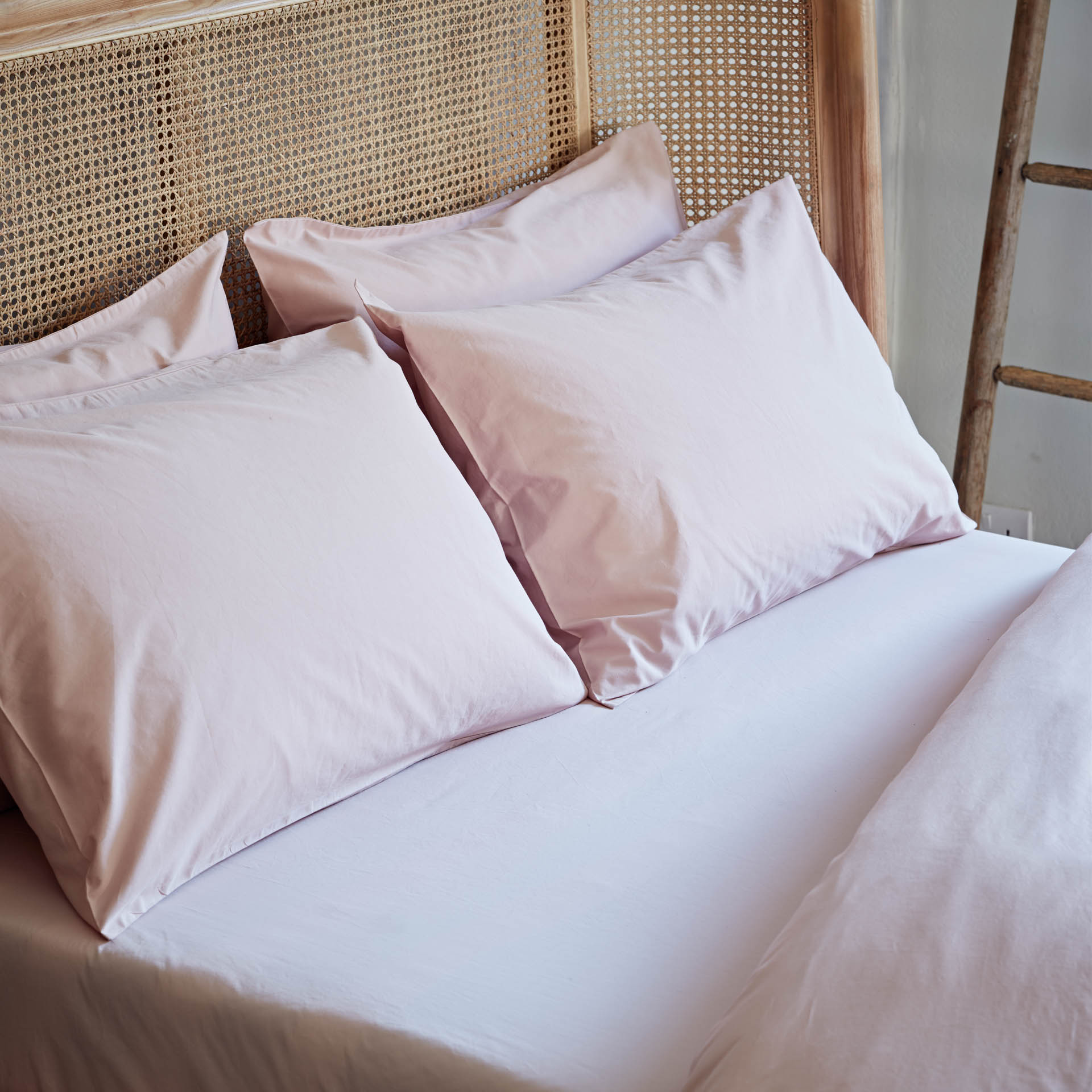 Pink pillows on a bed with a wicker headboard