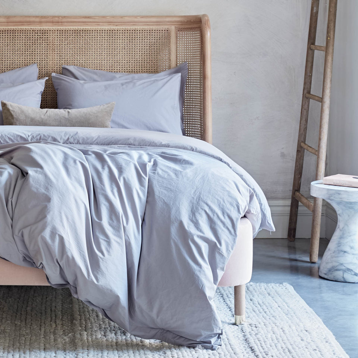 Bed with light gray bedding and pillows in a bedroom setting.