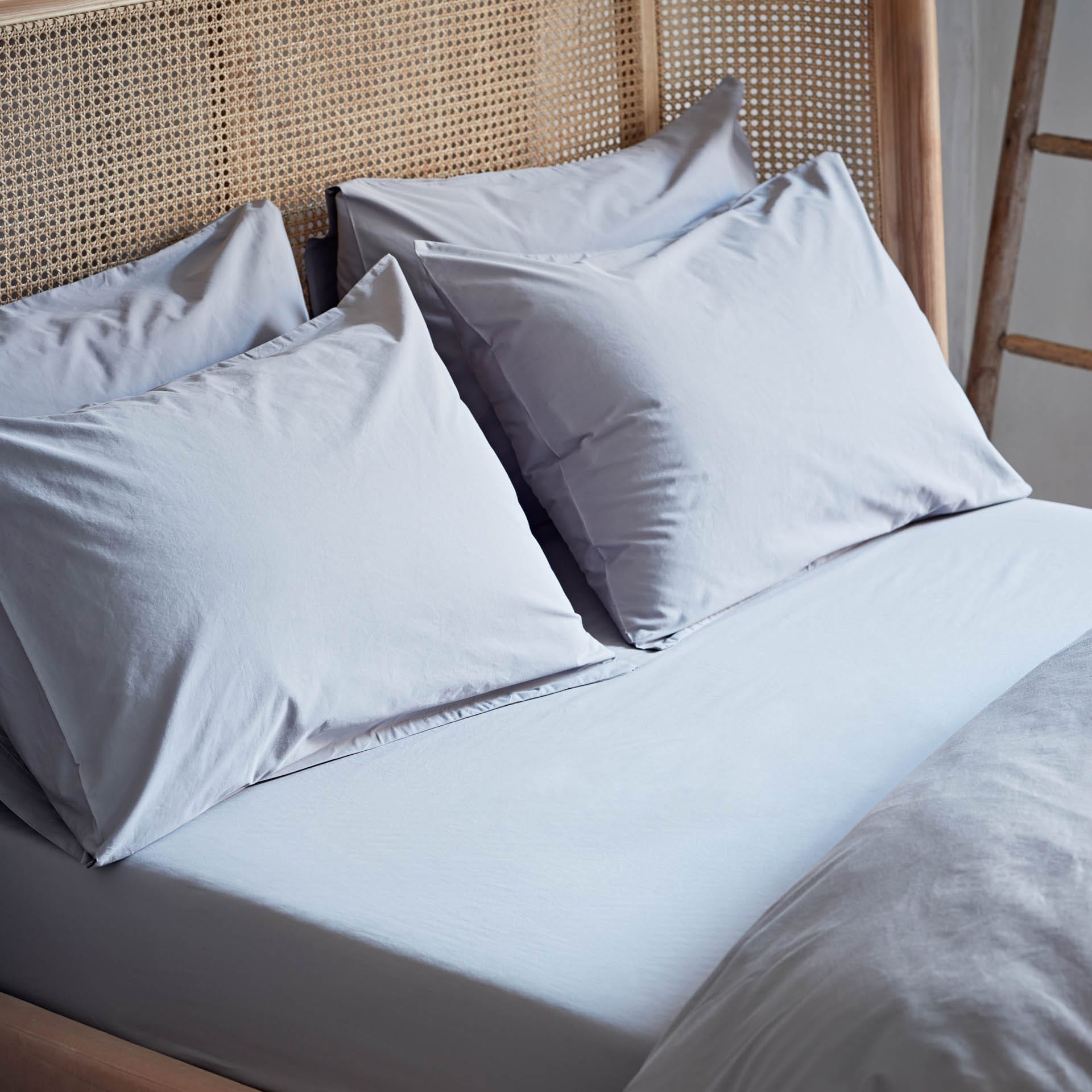 Light blue bedding set with pillows on a bed with a wicker headboard.