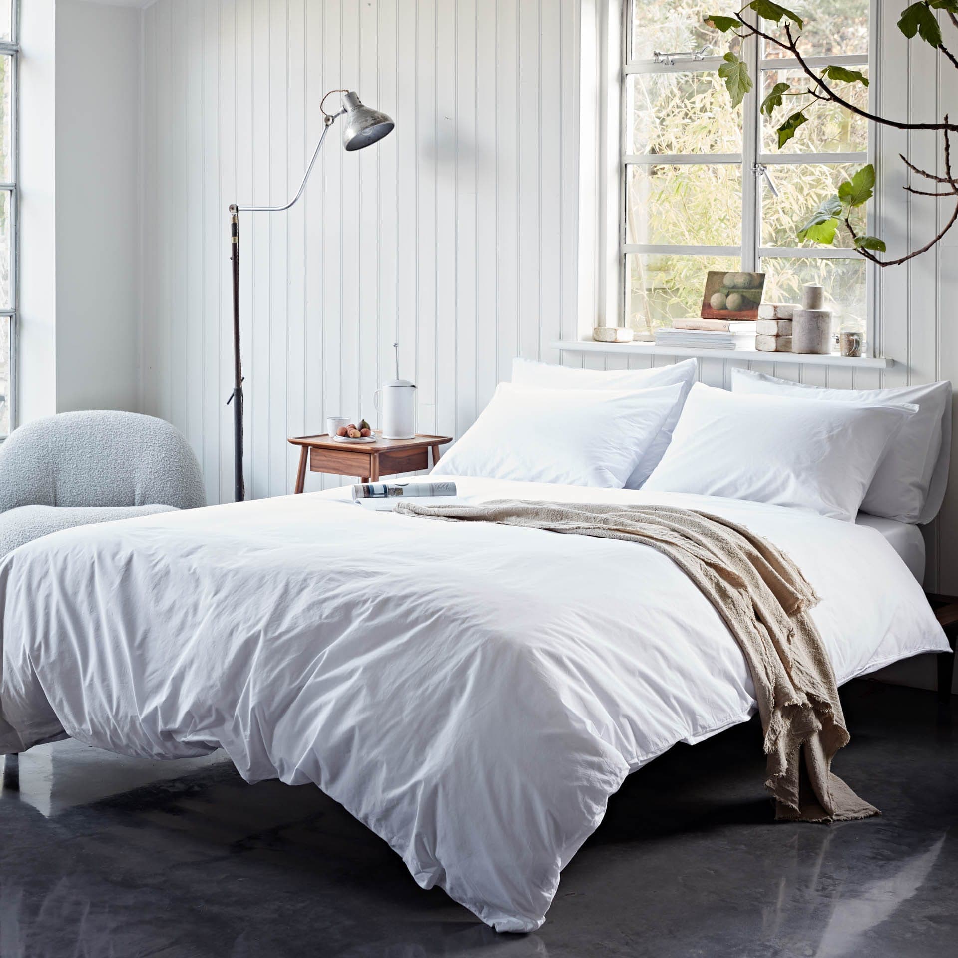 Neatly made bed with white bedding in a bright bedroom.