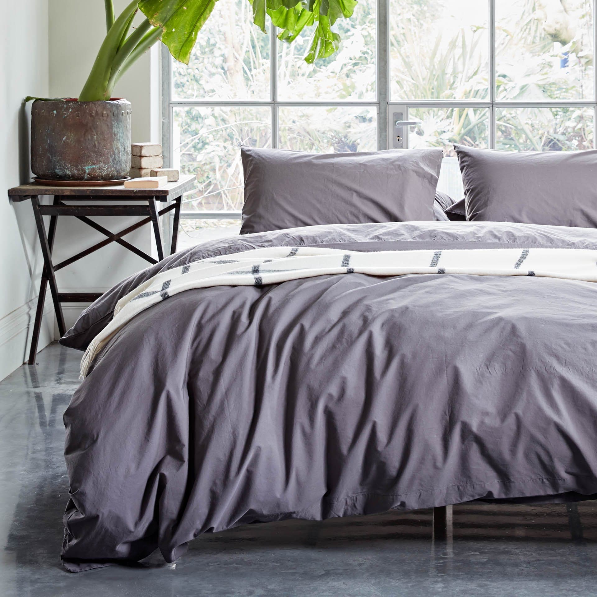 Gray bedding set on a bed with a window and plant in the background
