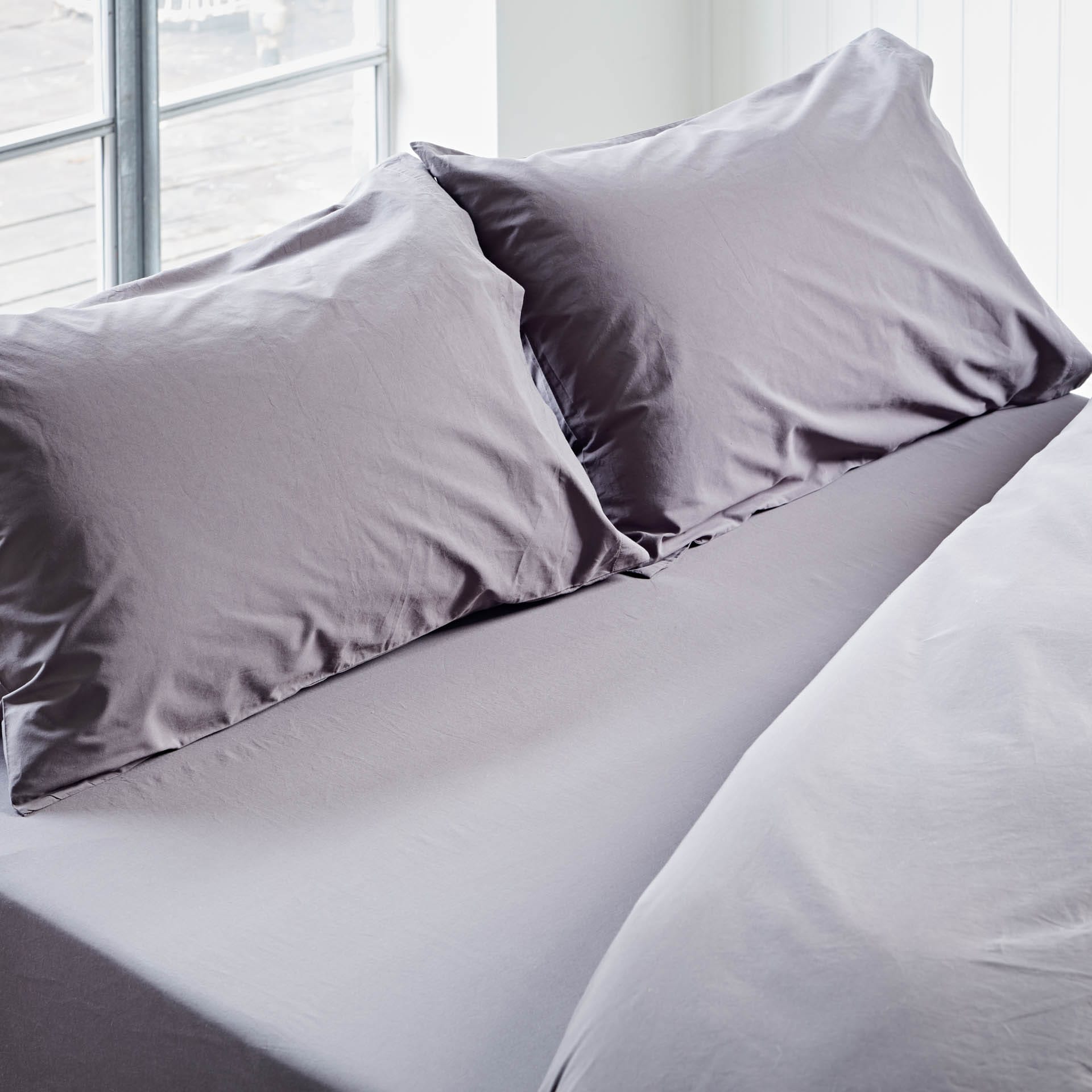 Gray bedding set with two pillows on a bed in a bright room.